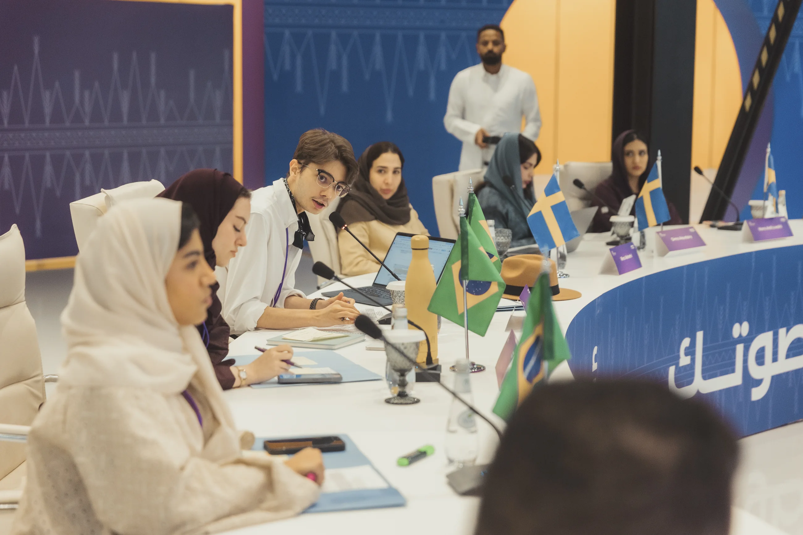 Sami Fathi seated at a roundtable with other participants and country flags